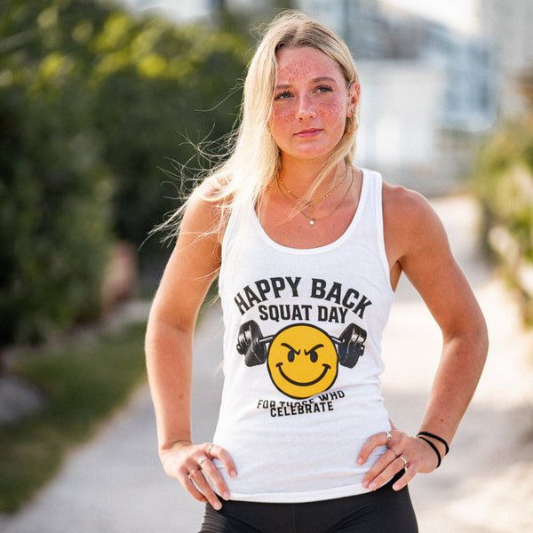 Woman wearing a tank top with 'Happy Back Squat Day' text and smiley face design outdoors.