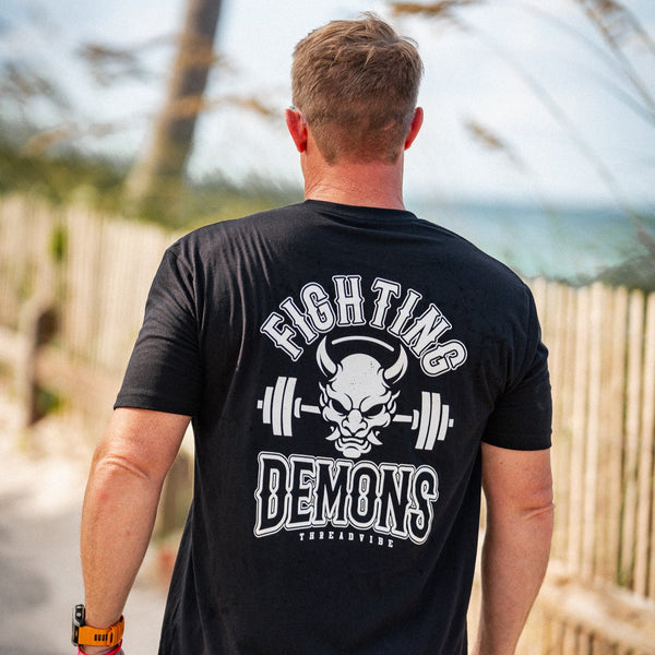 Man wearing a black t-shirt with 'Fighting Demons' design outdoors.