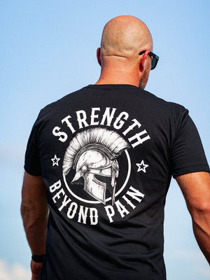 Man wearing a black t-shirt with 'Strength Beyond Pain' design against a blue sky.