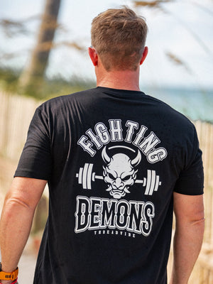 Man wearing a black t-shirt with 'Fighting Demons' design outdoors.